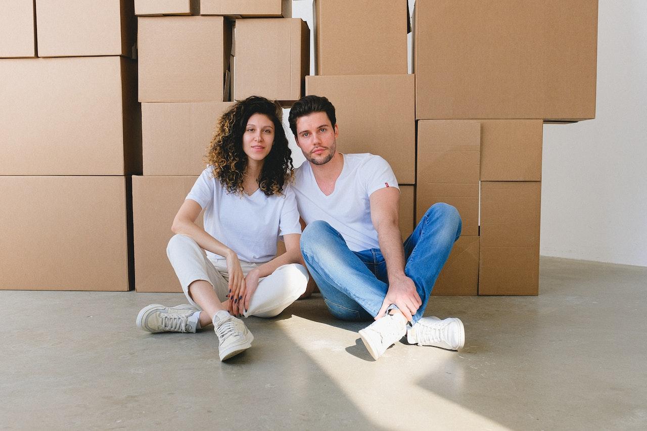 A man and a woman sit side by side with a lot of boxes behind them