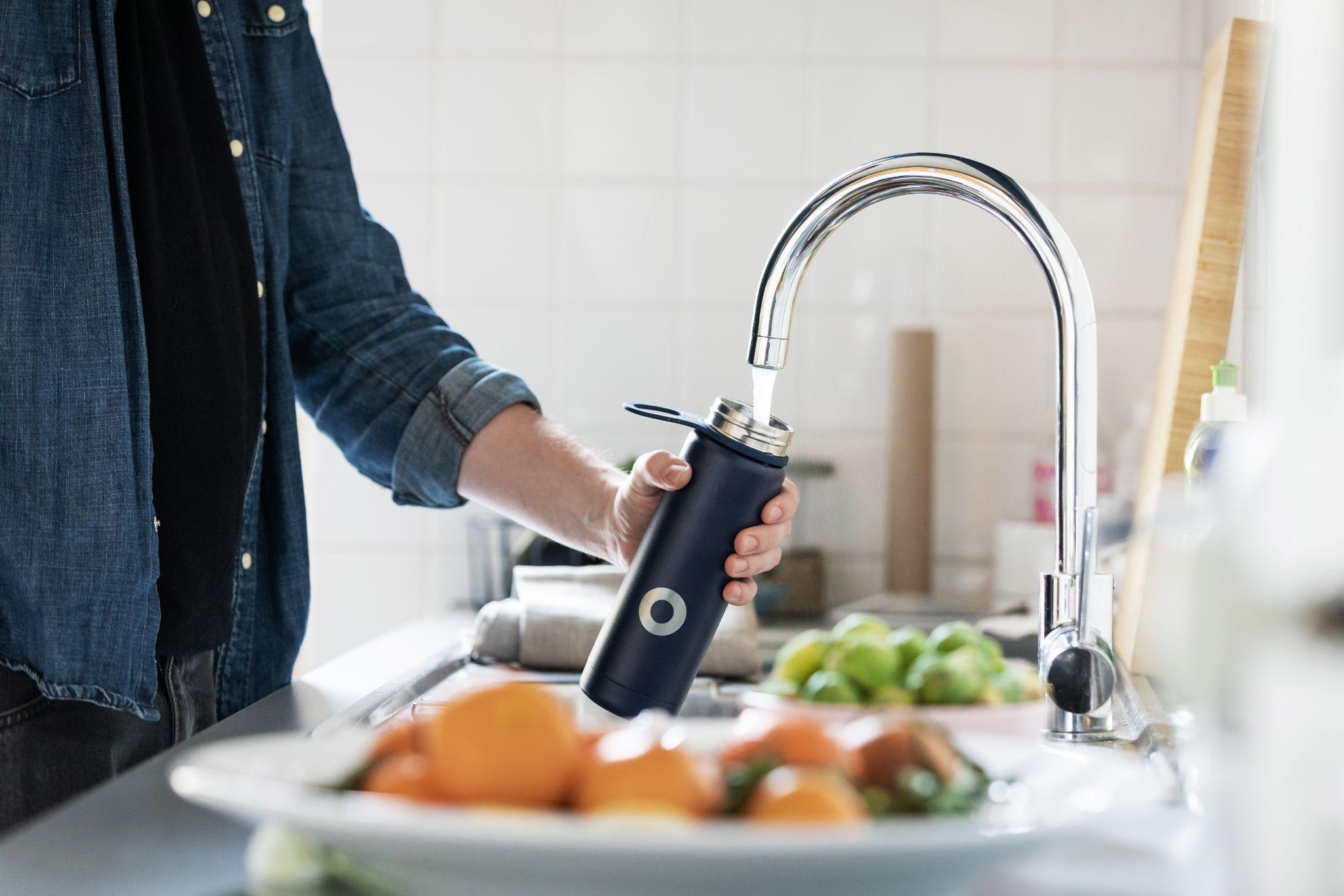 A man is holding a water bottle in front of a kitchen sink.