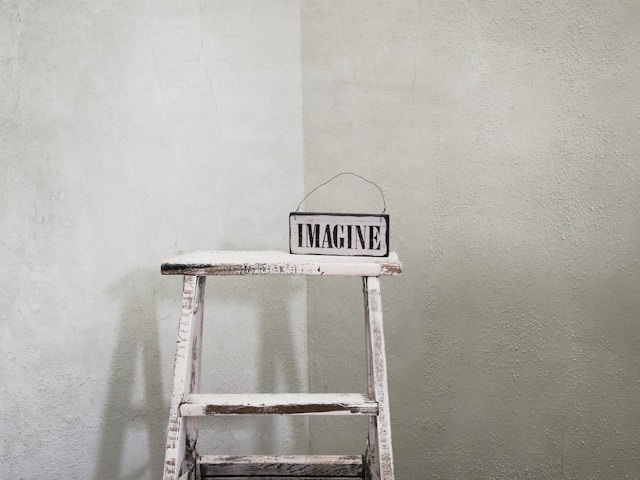 An old ladder turned into a rustic shelf with a sign saying "imagine" on it.